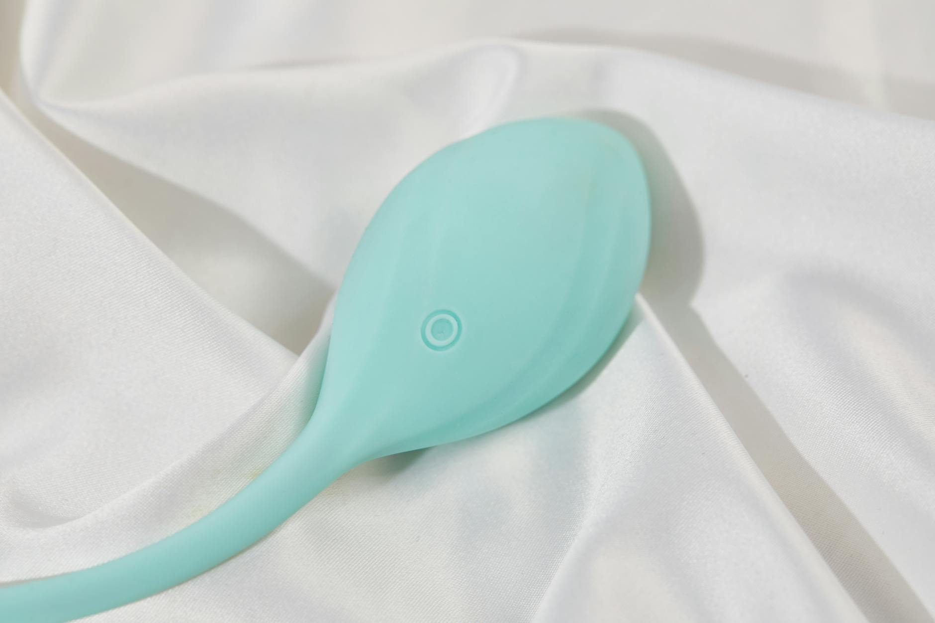 Vibrador de silicona en tonos teal sobre tela blanca suave