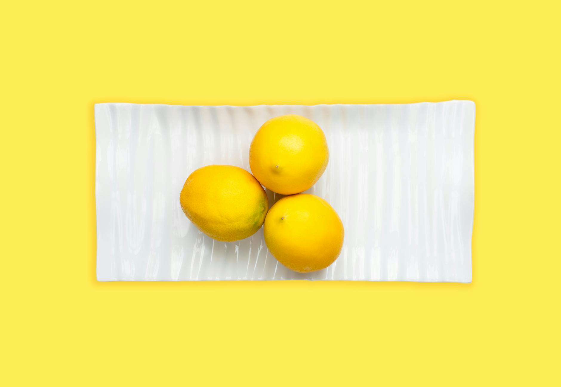 Limones frescos cortados en un plato blanco con fondo amarillo vibrante.