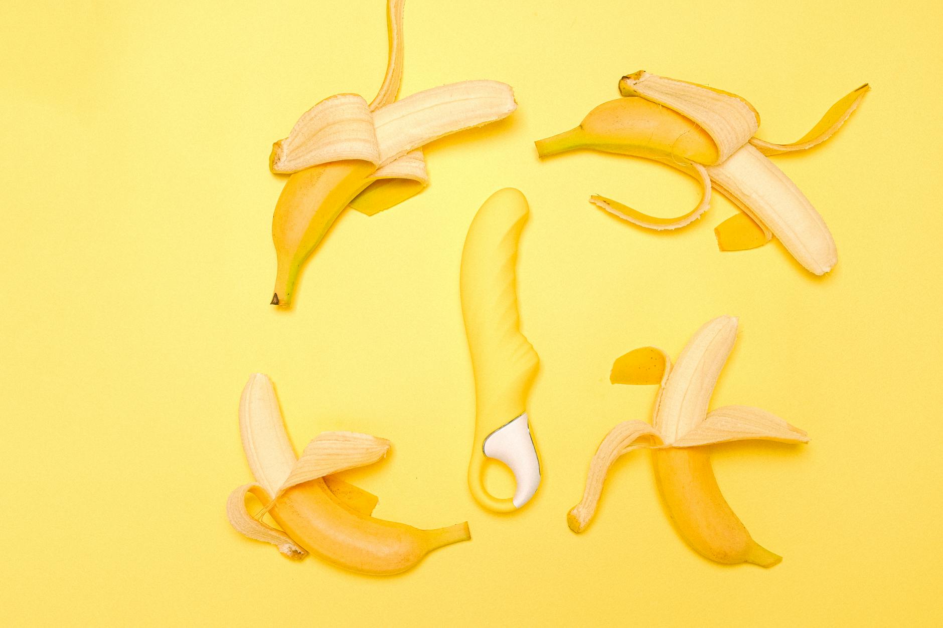 Yellow silicone lemon clitoral vibrator surrounded by peeled lemons on a bright yellow background.