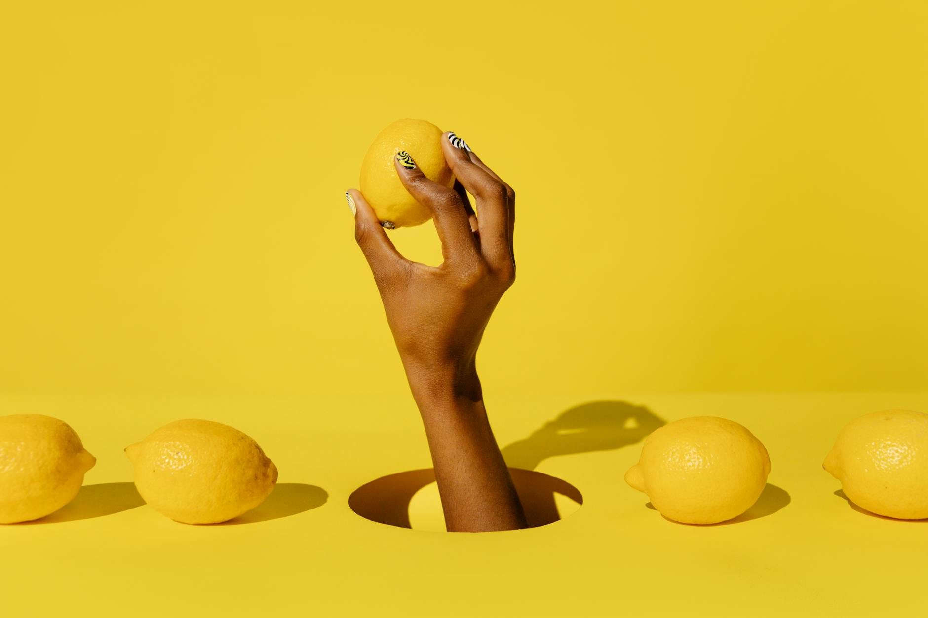 Una mano sosteniendo un limón fresco contra un fondo amarillo vibrante