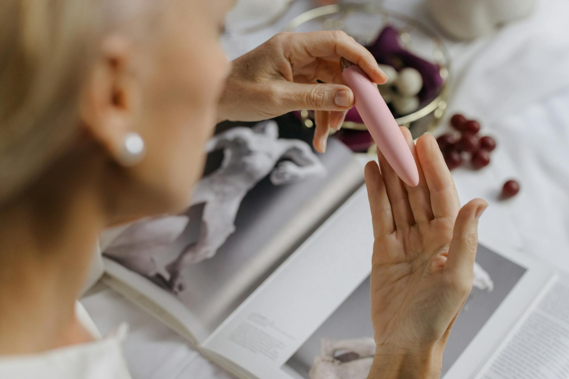Hand holding a pink vibrator with art books in background, emphasizing intimate personal themes