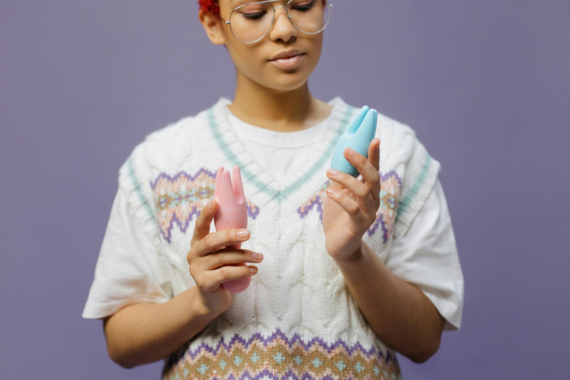 Woman with eyeglasses holding blue and pink silicone vibrators.